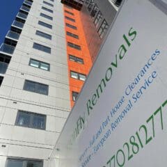 High-rise building with orange and white sections against a blue sky. In the foreground, a moving van is partially visible, displaying "DragonFly Removals" with contact details and services offered.